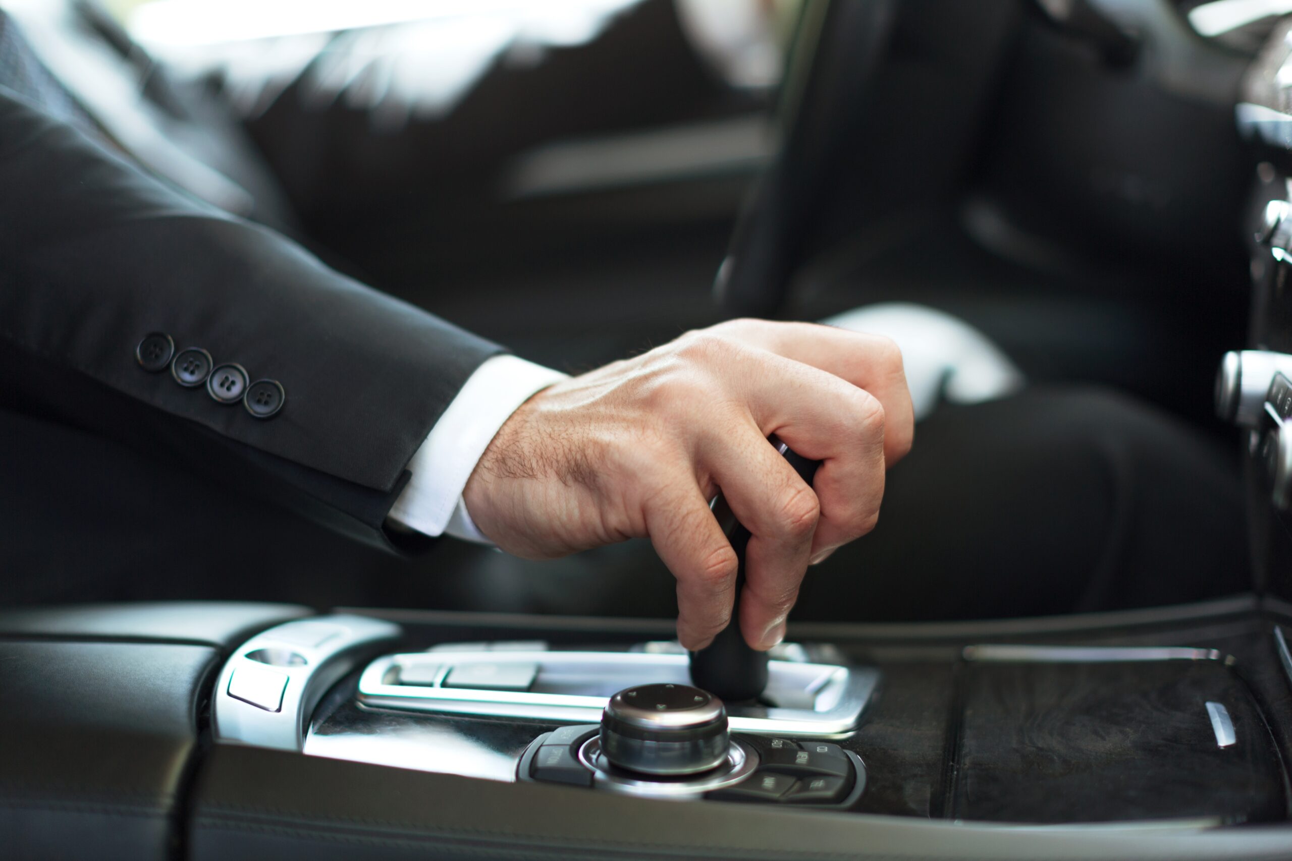 Businessman driving his car on background. Close-up human hand holding gear shift knob